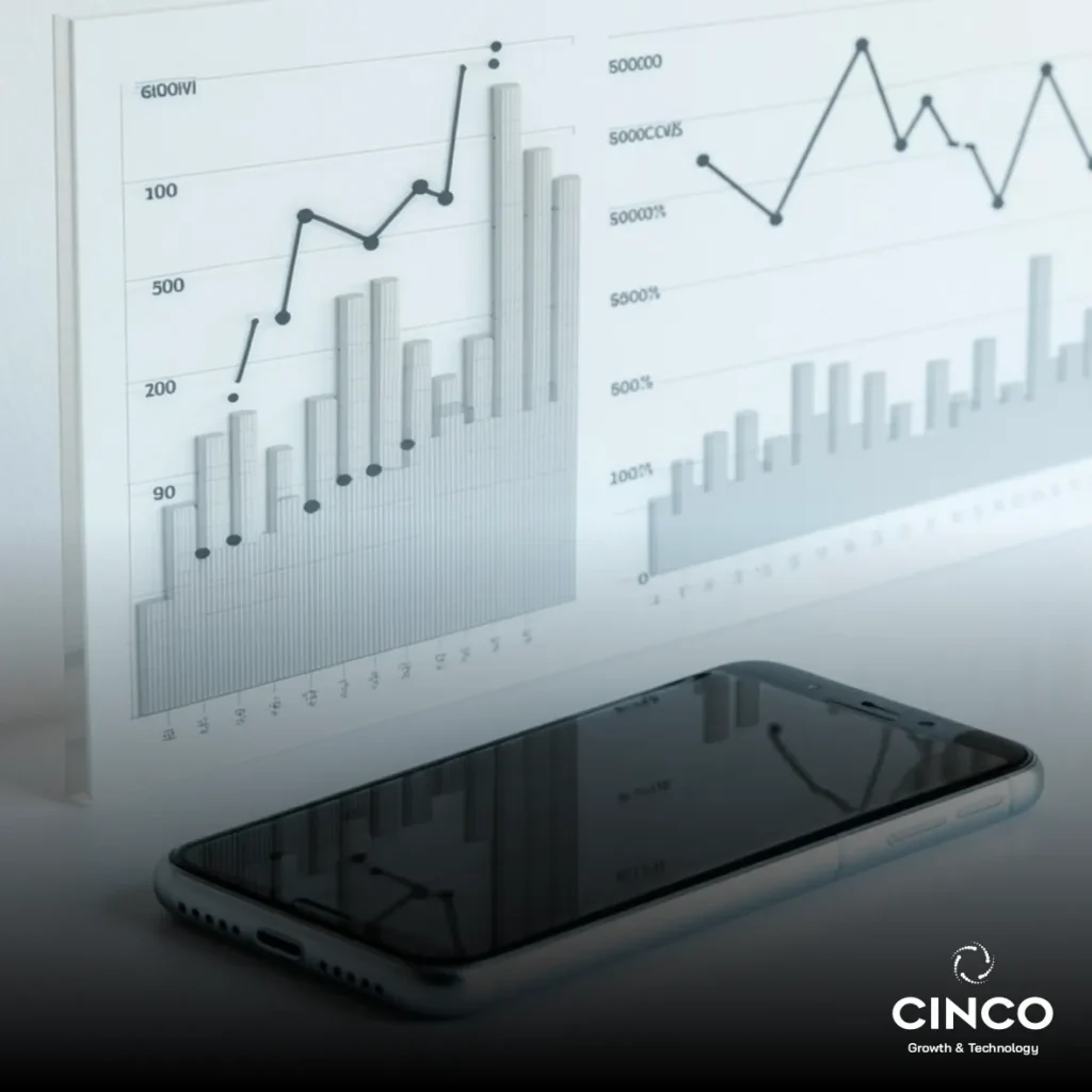 Um celular sobre a mesa e uma tela com gráficos abertos