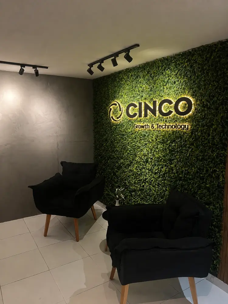 Recepção da Cinco Growth com parede verde, logotipo iluminado e poltronas pretas